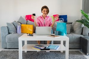 happy smiling woman in pink shirt on sofa at home shopping online